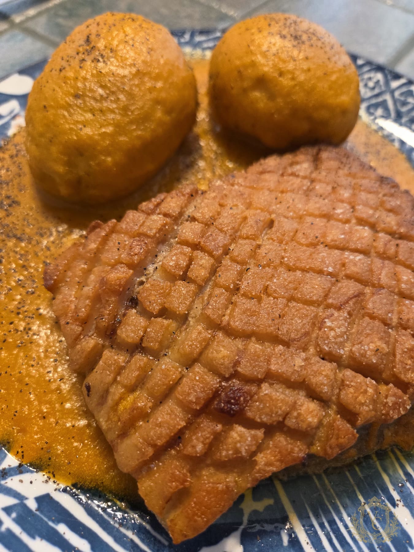 Close view of crisp pork belly with Yukon gold potatoes and orange pan sauce.